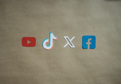 Four social media platform logos are arranged on a brown background. From left to right, the logos are for YouTube in red, TikTok in a combination of red, blue, and white, X in white, and Facebook in blue.