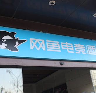 A building entrance features a vibrant blue sign with white Chinese characters and a stylized orca logo in black and white. The overall appearance suggests an establishment focused on eSports or digital activities.