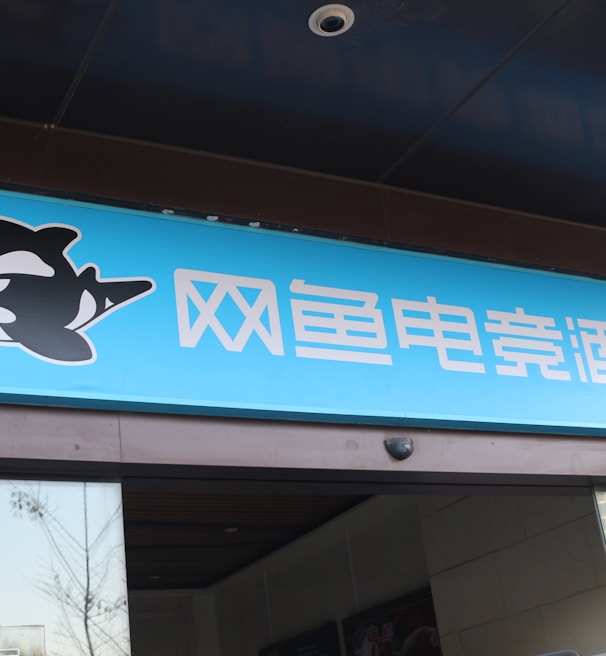A building entrance features a vibrant blue sign with white Chinese characters and a stylized orca logo in black and white. The overall appearance suggests an establishment focused on eSports or digital activities.